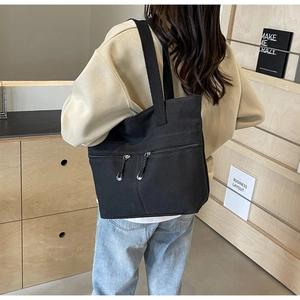Side view of large black canvas tote bag with front zippers on shoulder of model