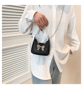 Detail of mini black sequin handbag with pearl chain handle and gold bow accent