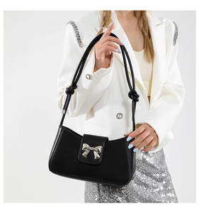 Detail of black underarm bag featuring a silver metal bow and knotted shoulder strap
