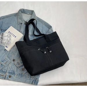 Detail of black canvas tote bag with dual front zipper pockets on denim background
