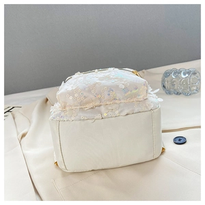 Detail eines weißen Pailletten-Rucksacks mit 3D-Blumenakzenten auf beigem Mantel-Hintergrund