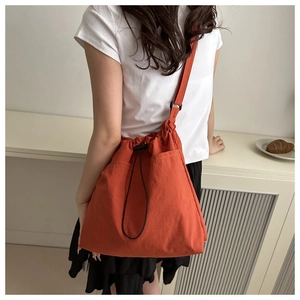 Detail of orange drawstring canvas crossbody bag showing multiple pockets and adjustable buckles