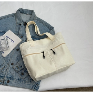 Detail of off-white canvas tote bag with front zipper pockets on a white lifestyle set