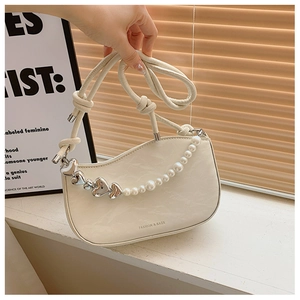 Detail of silver heart charm and white pearl chain on cream leather shoulder bag
