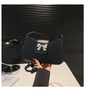 Detail of matte black underarm bag featuring a silver metal bow accent and shoulder strap