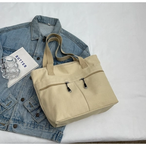Detail view of beige canvas tote bag with front double zippers and soft strap