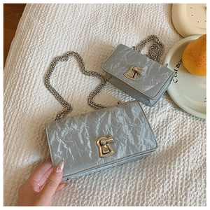 Detail of silver-grey pleated chain bags with silver rotary lock on white fabric