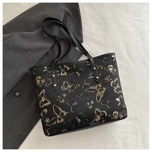 Detail of black tote bag featuring gold butterfly patterns and premium metal rivet straps
