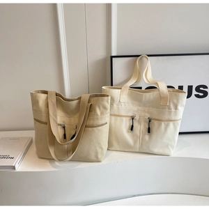 Detail of minimalist canvas tote bag featuring dual front vertical zipper pockets and handles