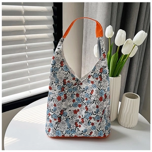 Gros plan du sac fourre-tout floral avec poignées orange sur une table blanche épurée