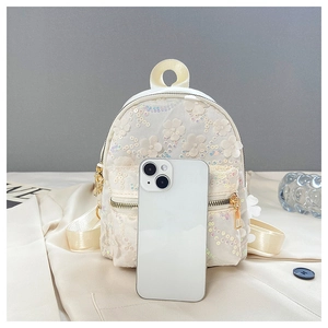Mini Rucksack in Weiß mit 3D-Blumen und Pailletten neben Smartphone für Größenvergleich