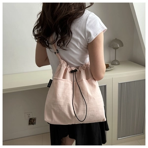 Detail of light pink drawstring tote bag showing front pocket and black adjustable cord