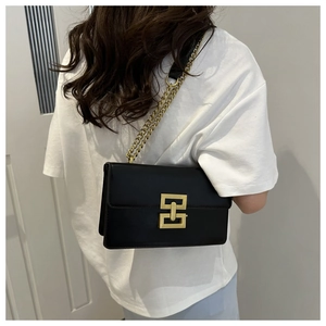 Detail of a black matte mini crossbody bag with a gold interlocking square buckle on a model
