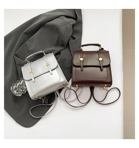 Silver and brown minimalist faux leather backpacks with gold buckles on a grey blazer