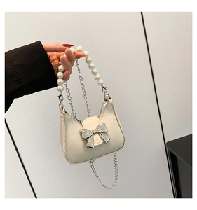 Detail of cream bow shoulder bag featuring pearl strap and silver metal bow ornament