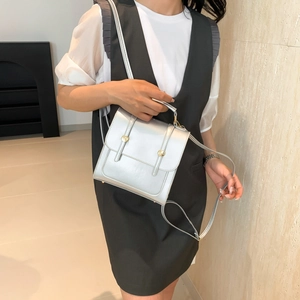 Silver metallic box bag with gold buckles and top handle worn by a model in a modern room