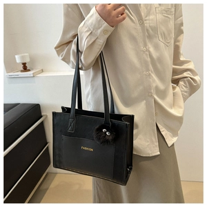 Detail view of black leather tote bag with gold fashion text and fluffy charm on model