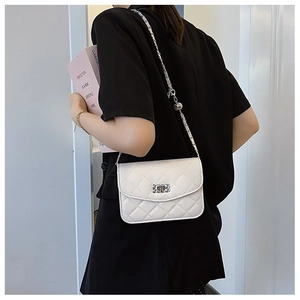 Close-up of a white quilted crossbody bag with a chain strap worn by a model in a casual setting