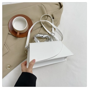 Détail d'un sac à main blanc géométrique avec poignée en métal argenté sur un blazer