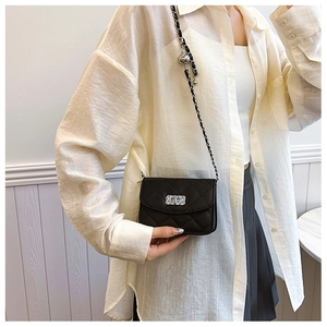 Detail of black quilted crossbody bag with silver lock and leather chain strap