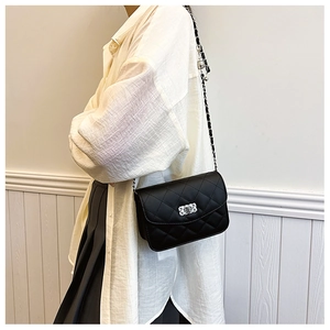 Detail of a quilted black crossbody bag with diamond square buckle worn by a model
