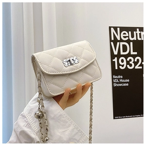 Detail of white quilted crossbody bag featuring metal turn-lock and chain strap with silver orb