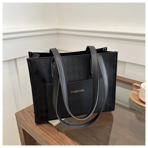 Close-up of black quilted tote bag featuring a front pocket and gold Fashion lettering