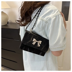 Side view of model wearing a black glossy crossbody bag with silver butterfly buckle