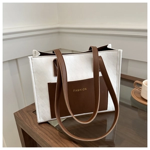 Detail of white quilted tote bag with brown leather pocket and gold FASHION text