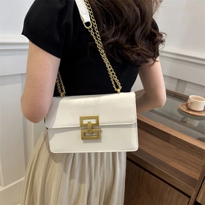 White faux leather crossbody bag with gold geometric buckle and chain strap on shoulder