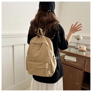 Detailed back view of a minimalist beige oxford fabric backpack worn by a model