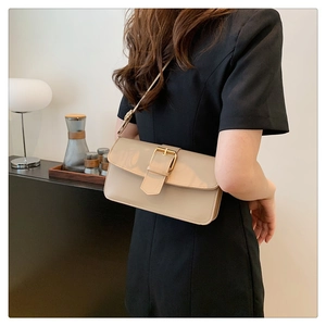 Detail of light beige crossbody bag with gold buckle on a model in modern interior
