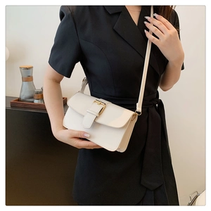 Detail of a minimalist ivory flap crossbody bag with gold buckle on a black blazer
