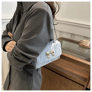 Detail of light blue pleated shoulder bag with golden bow clasp and silver chain strap