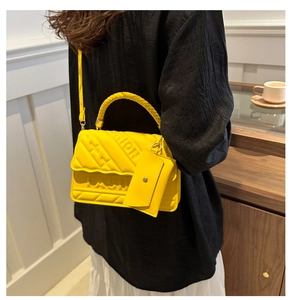 Detailed view of yellow quilted handbag with woven handle and small coin purse attachment