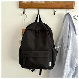 Detail of black oxford backpack with fashion label hanging on a wooden hook in a room