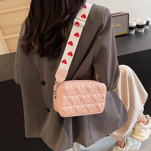 Pink heart quilted crossbody bag with red heart pattern wide strap worn on shoulder