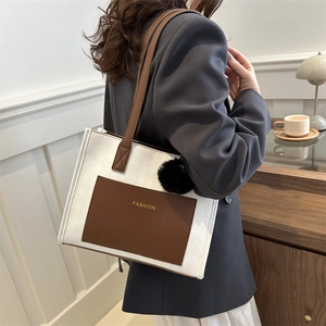 Minimalist white woven tote bag with brown leather pocket and black fur ball charm