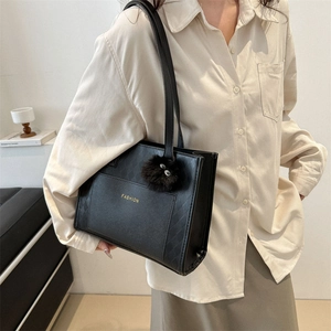 Chic black quilted tote bag with golden lettering and fluffy pendant on a model