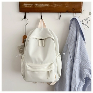 Detailed view of a minimalist beige oxford fabric backpack hanging on a wooden hook