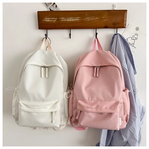 Detail view of cream and pink oxford backpacks hanging with side drawstring pockets