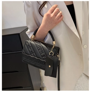 Detail of black quilted handbag with embossed FASHION logo and woven handle decoration