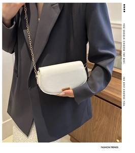 Detail of white leather saddle bag with gold chain strap and metallic hardware buckle