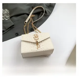 Détail du sac crème à motif crocodile avec boucle S dorée et pompon métallique
