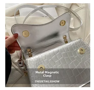 Close-up of silver crocodile embossed handbag with golden cylindrical magnetic buckle