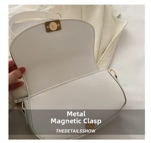Detail showing high-quality golden magnetic metal clasp on a white leather saddle bag