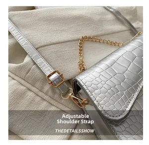Silver shoulder bag detail with crocodile texture, adjustable strap and gold metal buckle