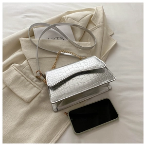 Silver crocodile embossed handbag with gold chain strap shown next to a smartphone
