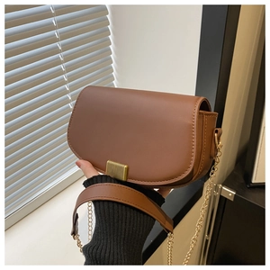 Close-up of a brown leather saddle bag with gold chain strap and magnetic flap closure