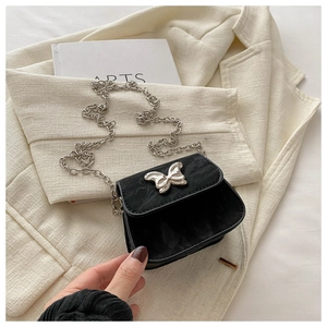 Détail de la boucle papillon argentée et de la texture noire mate sur ce mini sac à chaîne